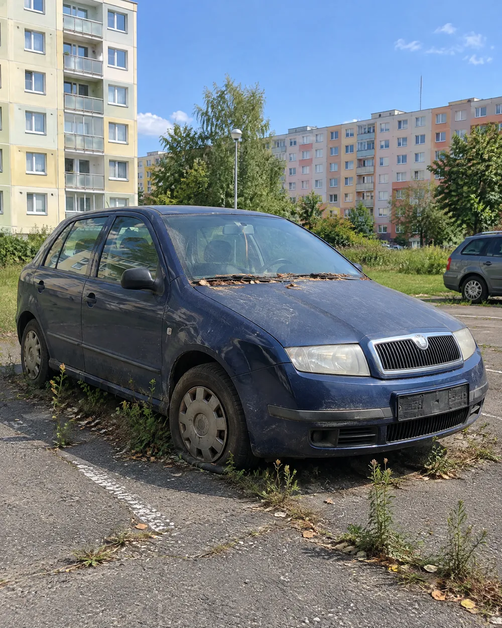 Dlouho stojící Škoda Fabia s prázdnou pneumatikou na sídlištním parkovišti